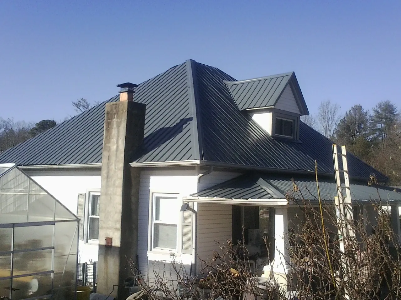 Dark blue standing seam metal roof on a white farmhouse with dormer — Slate & Tile Roof Repair by Roofing Brothers in Dewey