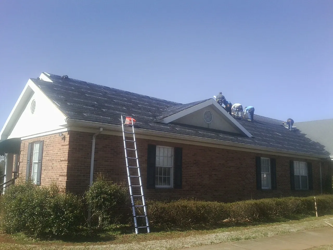 Crew tearing shingles off a brick ranch roof with a ladder set — Emergency Roof Repair work by our crew in Dewey