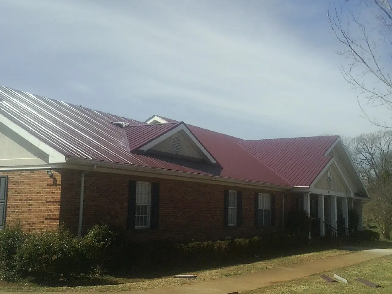 Red metal roof with gabled entries on a long brick building, from a Hail Damage Roof Repair job in Dewey
