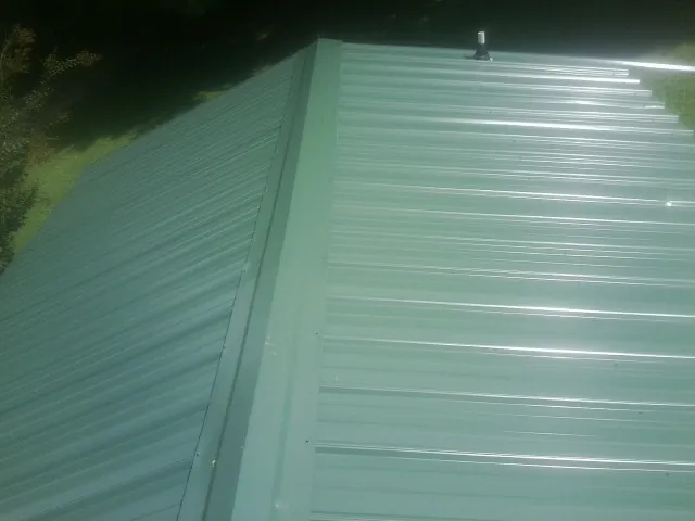 New green metal panels meeting at the ridge of a roof — Flat Roof Repair work by our crew in Dewey