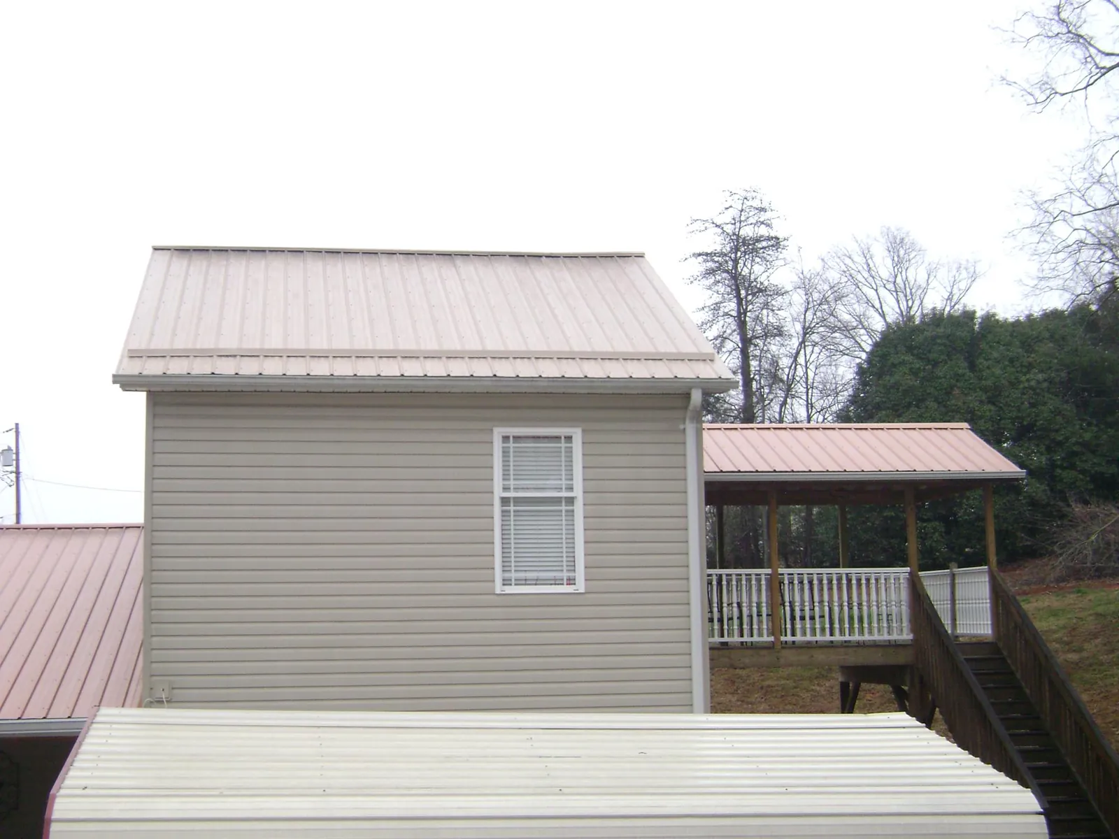 Tan metal roofs on a two story addition and attached porch, from a Roof Replacement job in Dewey