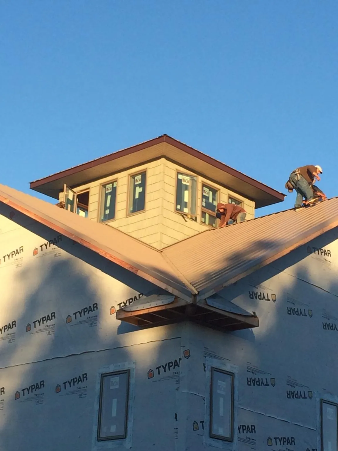 Roofers working around a rooftop cupola on a new metal roof at sunset — Roof Waterproofing in Dewey by Roofing Brothers